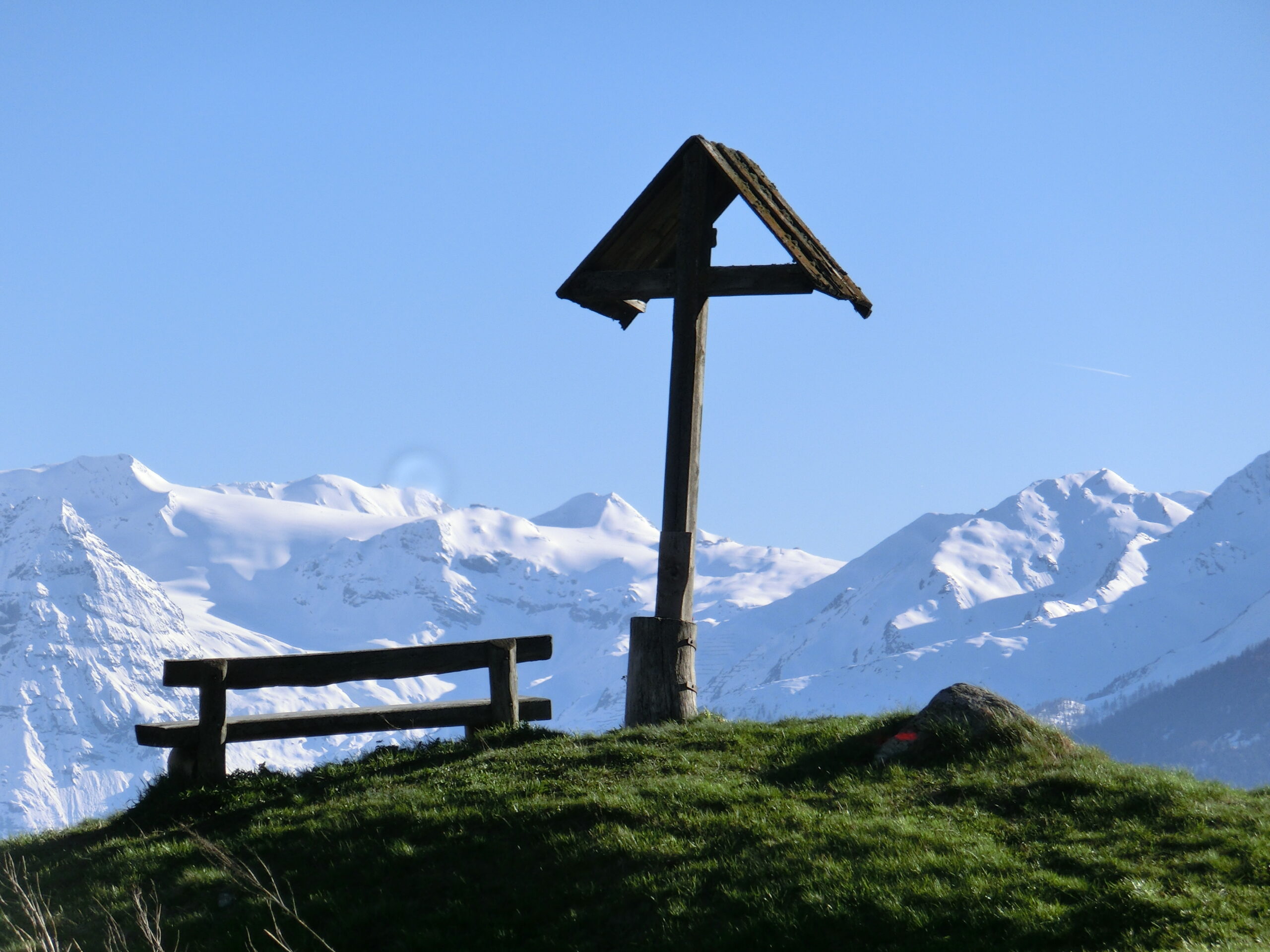 Holzkreuz auf Almwiese mit schneebedecktem Bergpanorama im Vinschgau in Südtirol