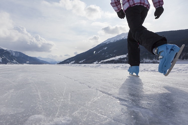 Person beim Eislaufen auf gefrorenem See im Vinschgau mit Bergkulisse in Südtirol